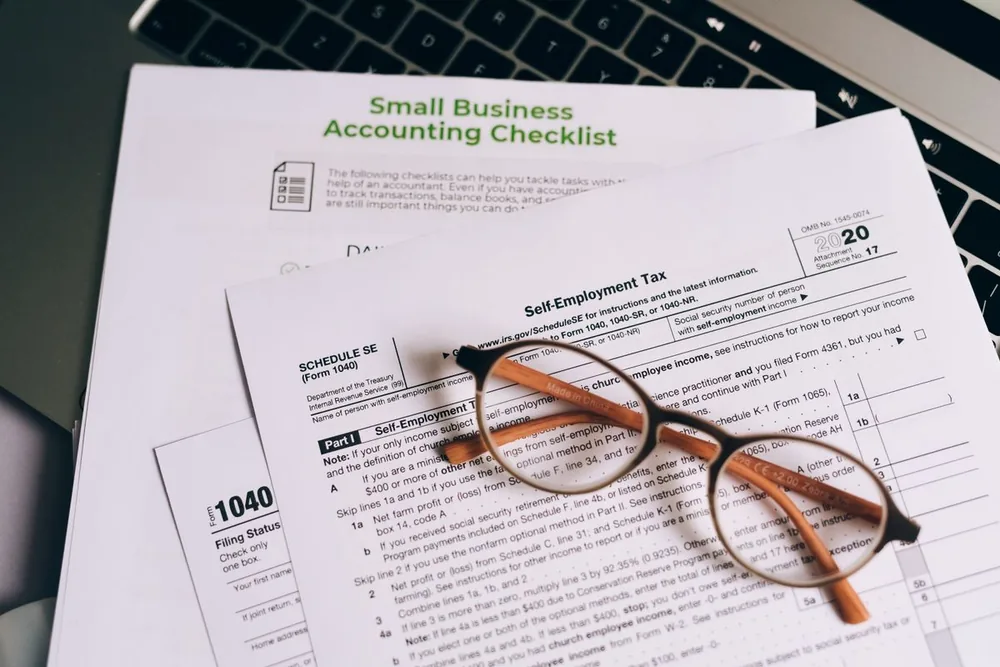 A small business accounting checklist and a Form 1040 with reading glasses resting on them.